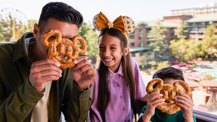 A man and boy hold Mickey shaped pretzels over their faces while a girl laughs between them