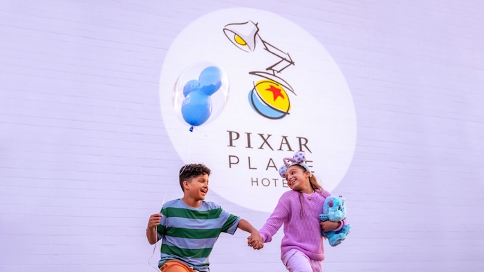 At Pixar Place Hotel, 2 kids skip together while one child holds a balloon and the other child holds a plush