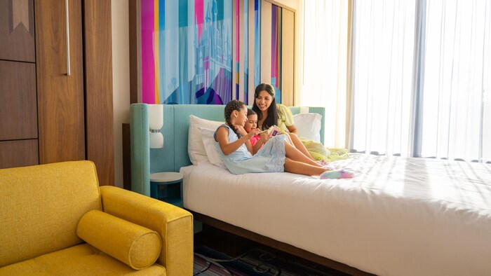 A mother and her 2 children lounge on a hotel bed at the Disneyland Resort