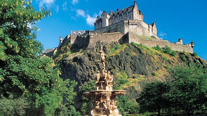Une statue complexe devant une falaise herbeuse avec un grand manoir en briques