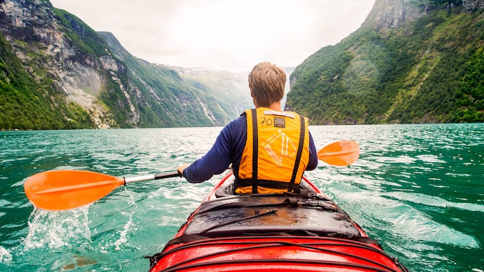 Homme assis dans des pagaies de kayak sur une eau calme entre des collines luxuriantes
