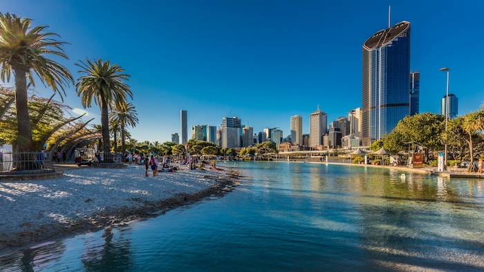 Une rivière tranquille avec une plage tropicale d’un côté et une ville cosmopolite de l’autre