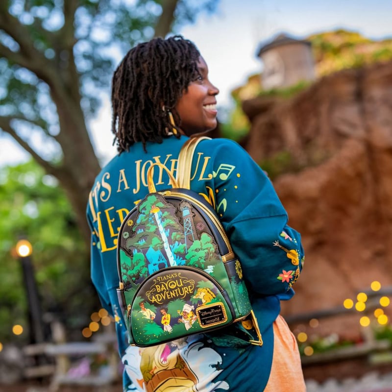 A woman with her back turned, wearing a Tiana's Bayou Adventure Loungefly Mini Backpack and a jersey