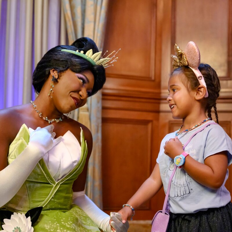 Princess Tiana holds hands with a girl wearing a Tiana’s Bayou Adventure ear headband 