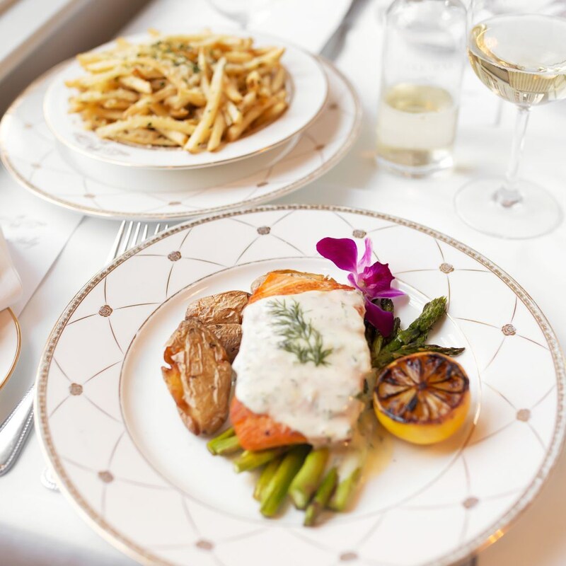 A dining table with a plate of french fries, a glass of wine and a plate of salmon, asparagus and potatoes