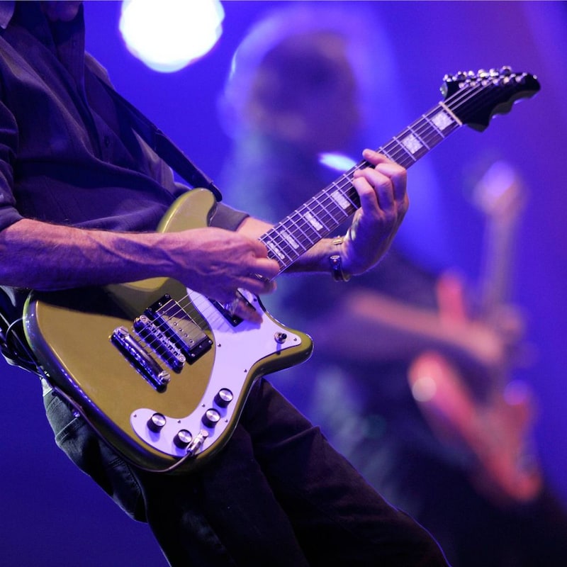 Un guitarrista toca en el frente del escenario junto a otro músico que toca el bajo