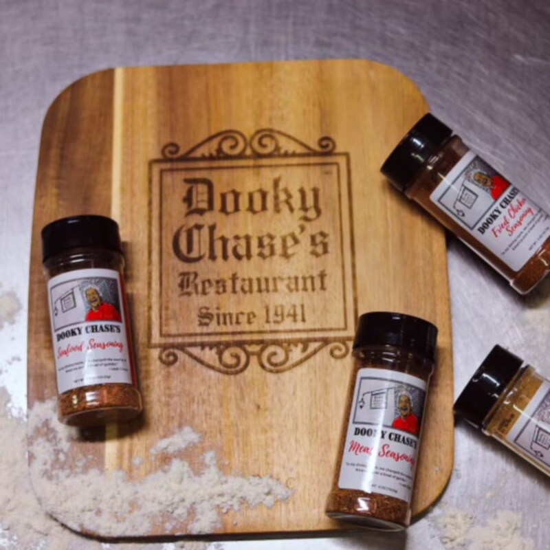 Quatro vidros de tempero sobre uma tábua de cortes com os dizeres “Dooky Chase’s Restaurant desde 1941”, em inglês