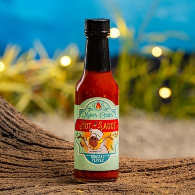 Um vidro do molho de pimenta Mama Odie’s Roasted Pepper Hot Sauce em um tronco 	