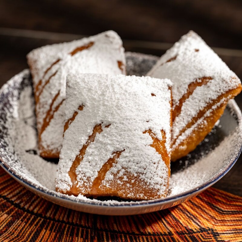 Três beignets cobertos com açúcar de confeiteiro, servidos em uma tigela