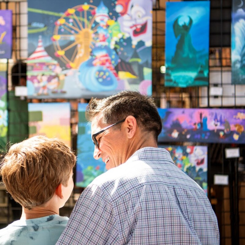 An adult and child gazing at artwork on display featuring various Disney characters