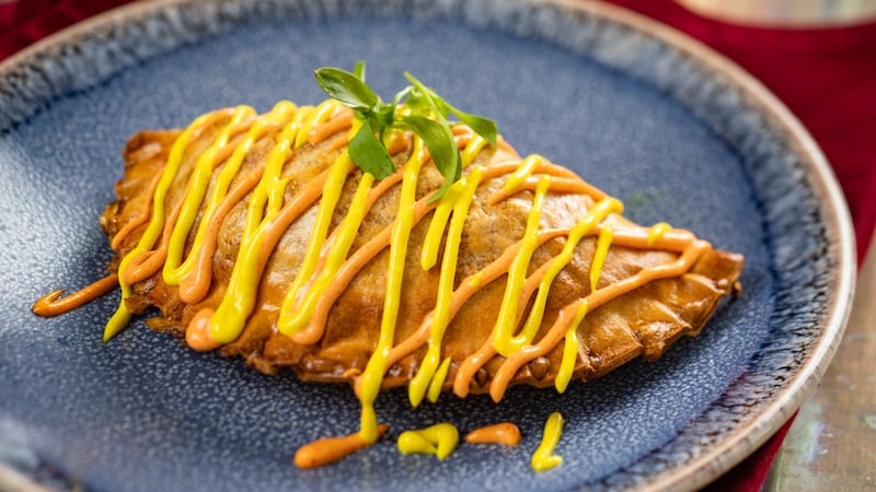 The Chorizo Potato Empanada drizzled with sauce and topped with fresh herbs