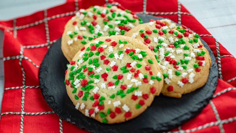 Three holiday sugar cookies covered in sprinkles on a stone plate