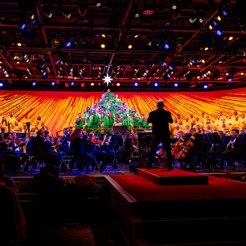 A conductor directing an orchestra and a choir, with some choir members dressed and arranged to look like a Christmas tree at the Candlelight Processional
