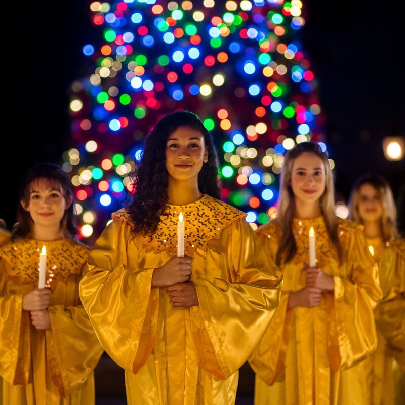 Un coro sostiene velas por la noche frente a un árbol de Navidad iluminado