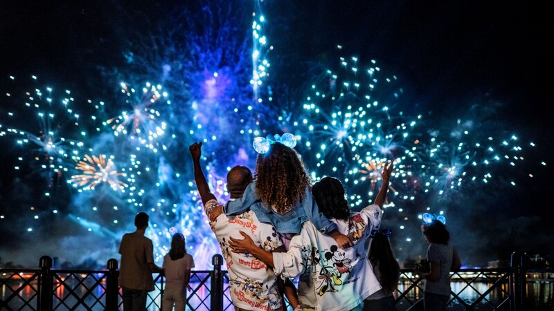 Two parents holding their young daughter up in the air as they watch a fireworks show at Epcot
