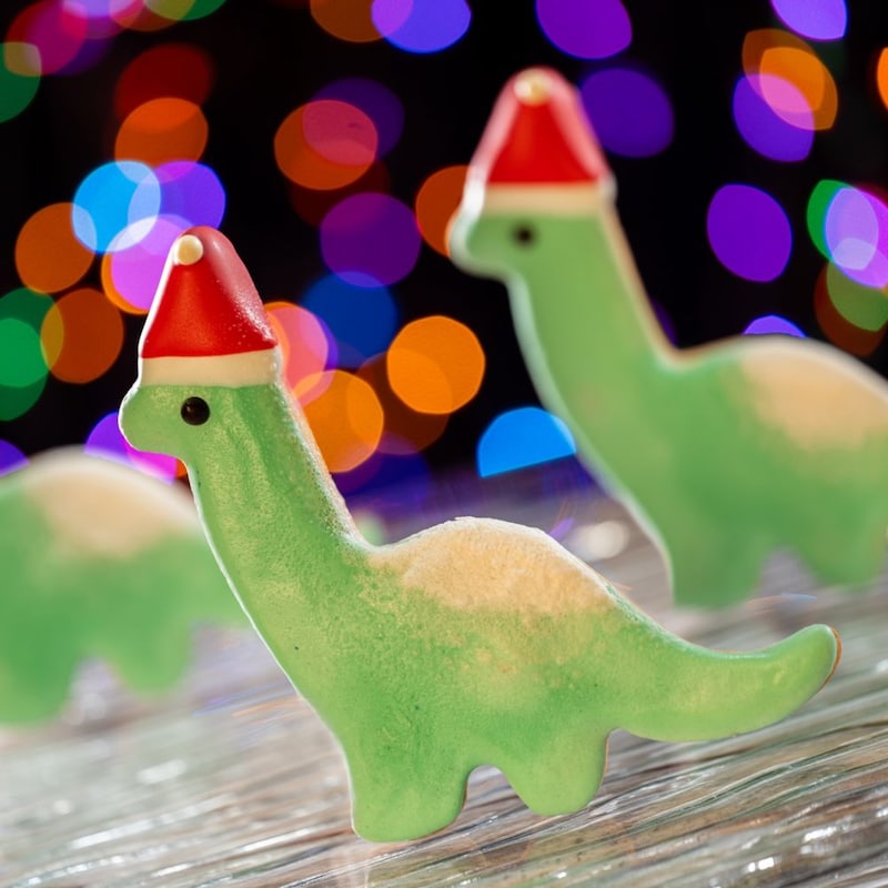 Tres galletas navideñas con forma y decoración de Gertie the Dinosaur con un sombrero de Santa Claus