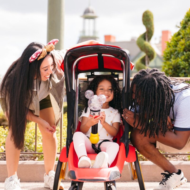 2 parents look on as their child beams from the seat of a rented stroller at Walt Disney World Resort