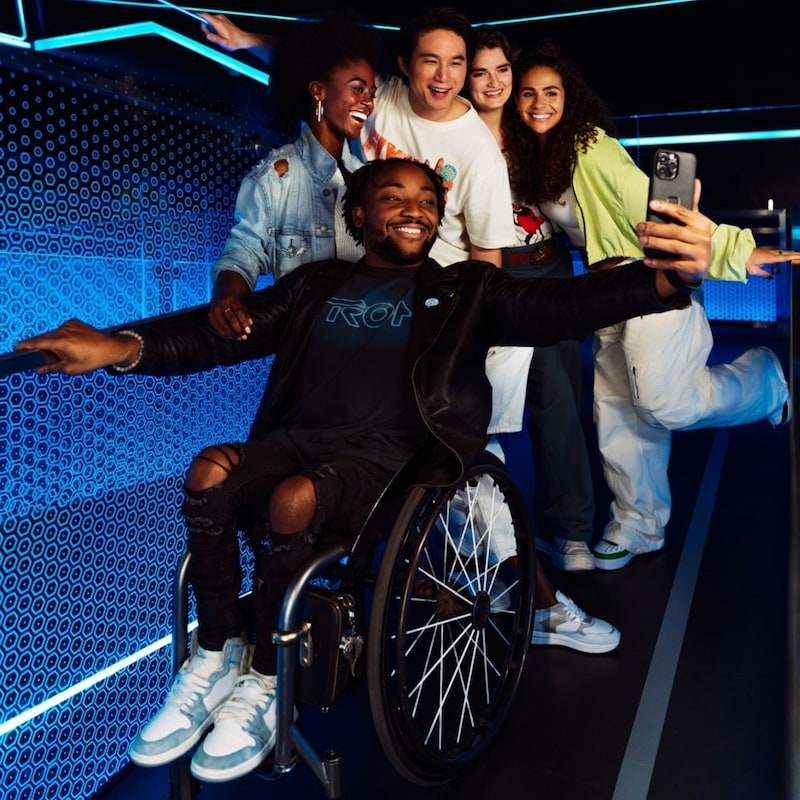 A man in a wheelchair and his friends posing for a photo at the TRON Lightcycle Run attraction