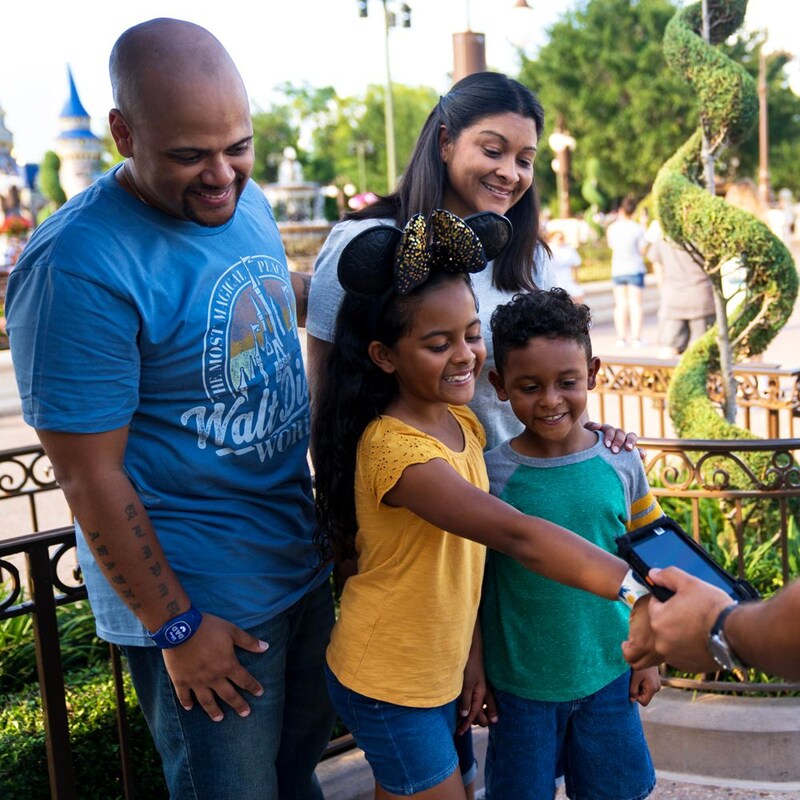 A little girl stands with her family and uses her Disney band in Magic Kingdom park