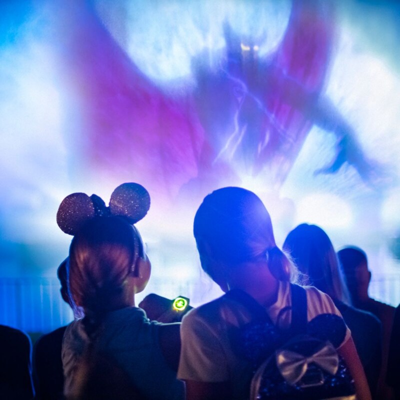 Two young Guests look at a glowing Disney band and watch a fireworks display featuring the Horned King