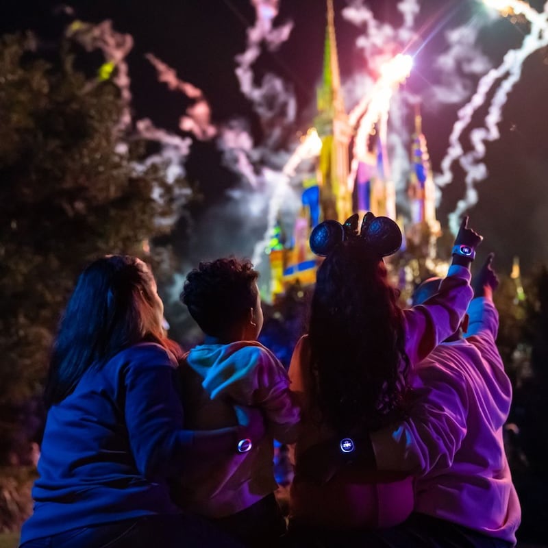 A family watches fireworks as the MagicBand Plus on each of their wrists glows