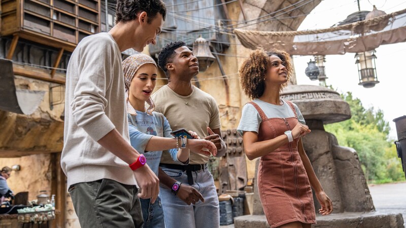 Un pequeño grupo de Visitantes mira sus MagicBands y un dispositivo móvil mientras se divierten con un juego en Star Wars Galaxy’s Edge