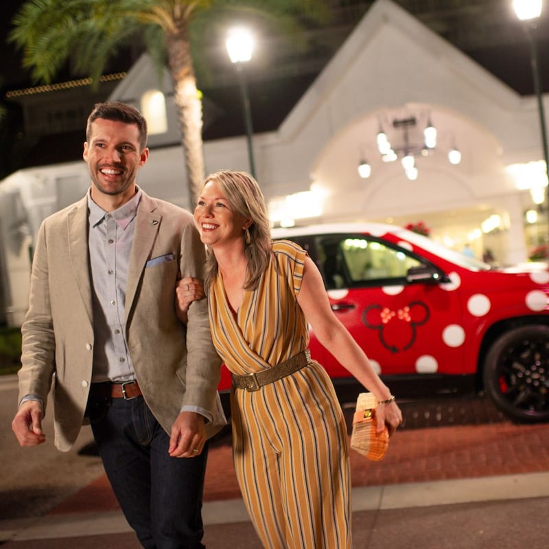 Un homme et une femme portant une tenue de ville passent devant un VUS Minnie Van à l’entrée d’un hôtel Disney