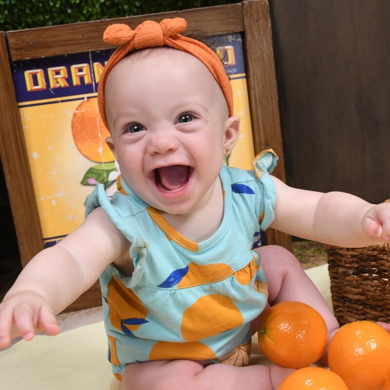 A baby posing with a basket of oranges