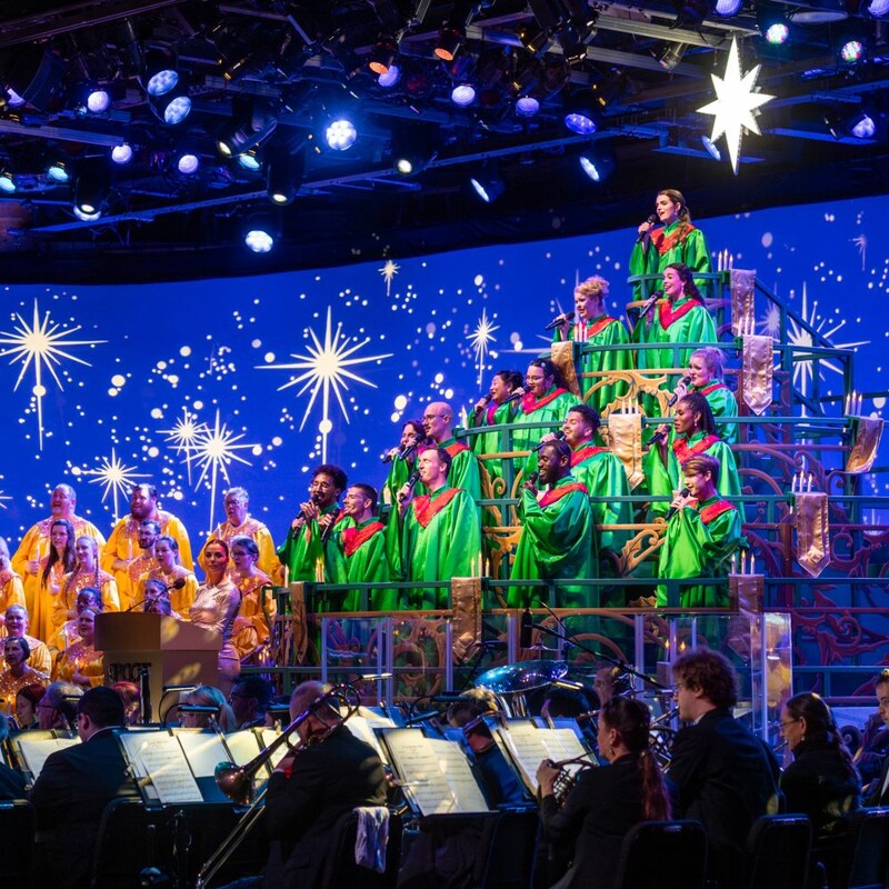Cantantes con vestimenta con temática festiva y una orquesta tocando en Candlelight Processional en EPCOT
