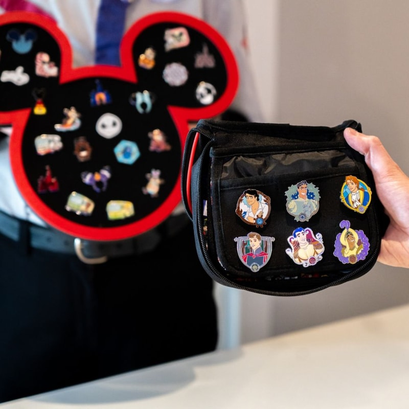 A Guest holding a Disney character pin trading bag near a Mickey Mouse shaped pin board