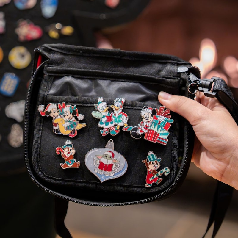A hand holding a bag of Disney holiday pins, with a Mickey-shaped pin trading board in the background