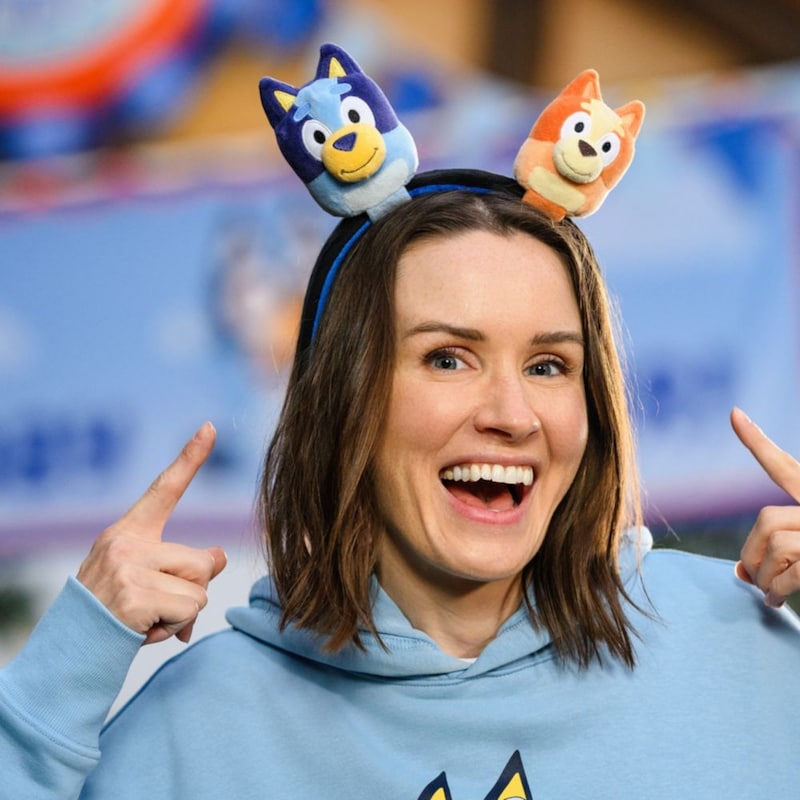 A woman pointing to a Bluey and Bingo plush headband, available during Bluey's Best Day Ever