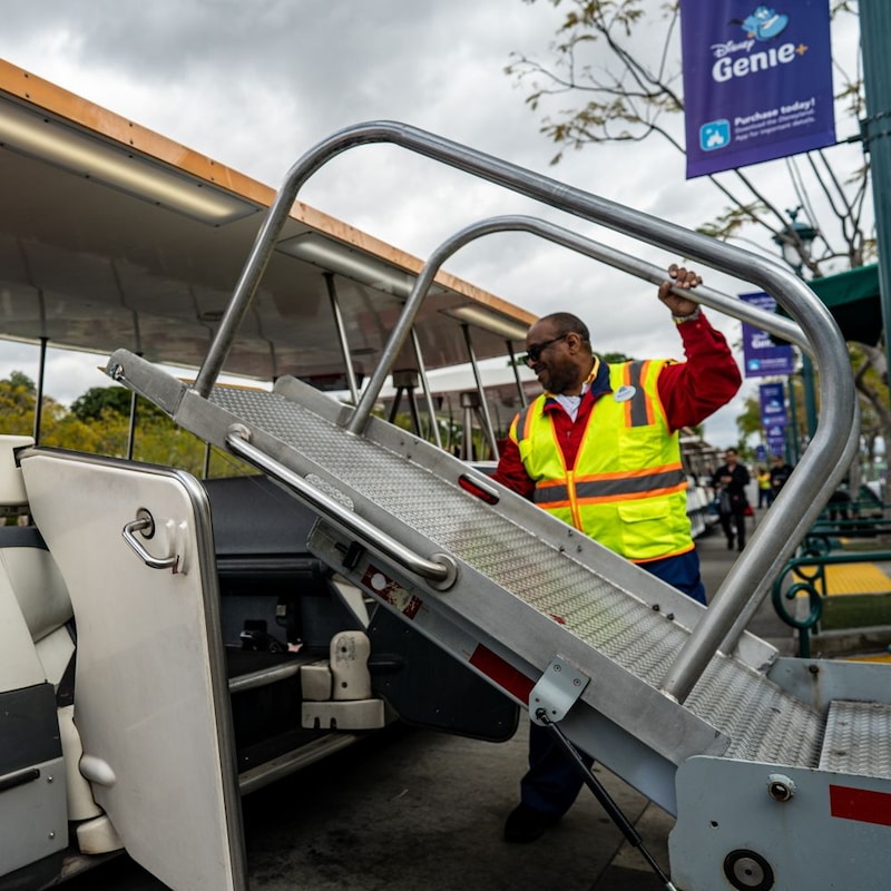 A parking Cast Member lowers a wheelchair ramp onto the tram