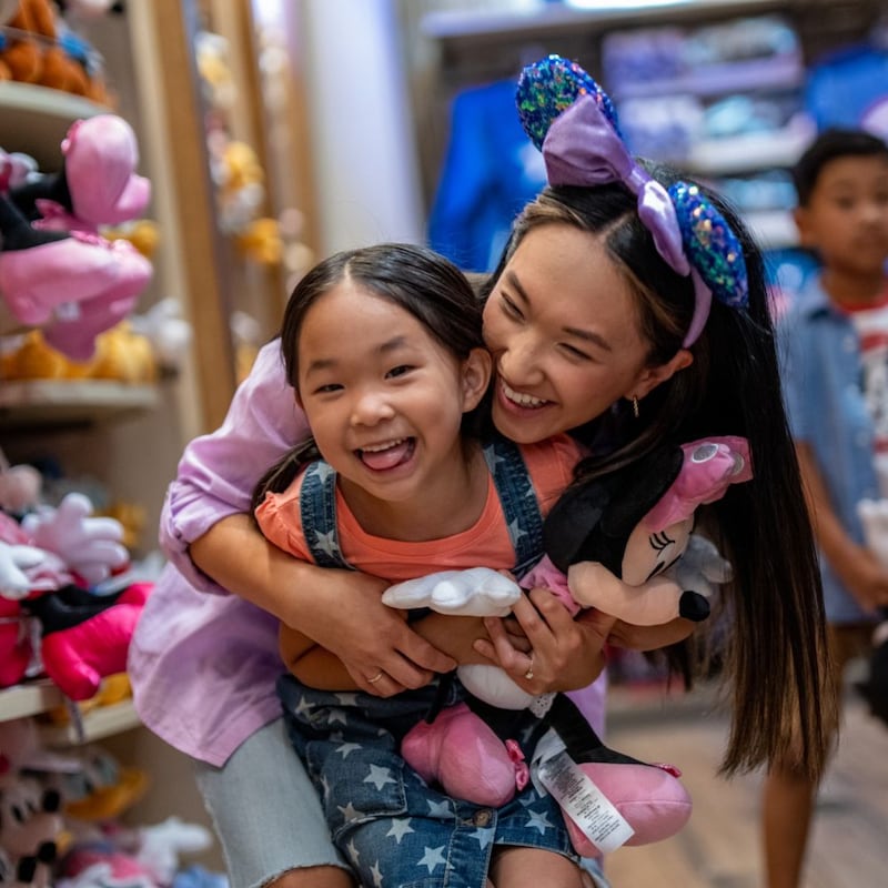 An older child gives a playful hug to a younger child who is holding a Minnie Mouse plush toy