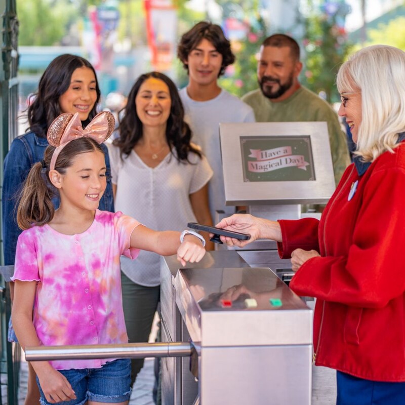 A child tapping a Magic Band Plus to a phone at a Disney theme park entrance