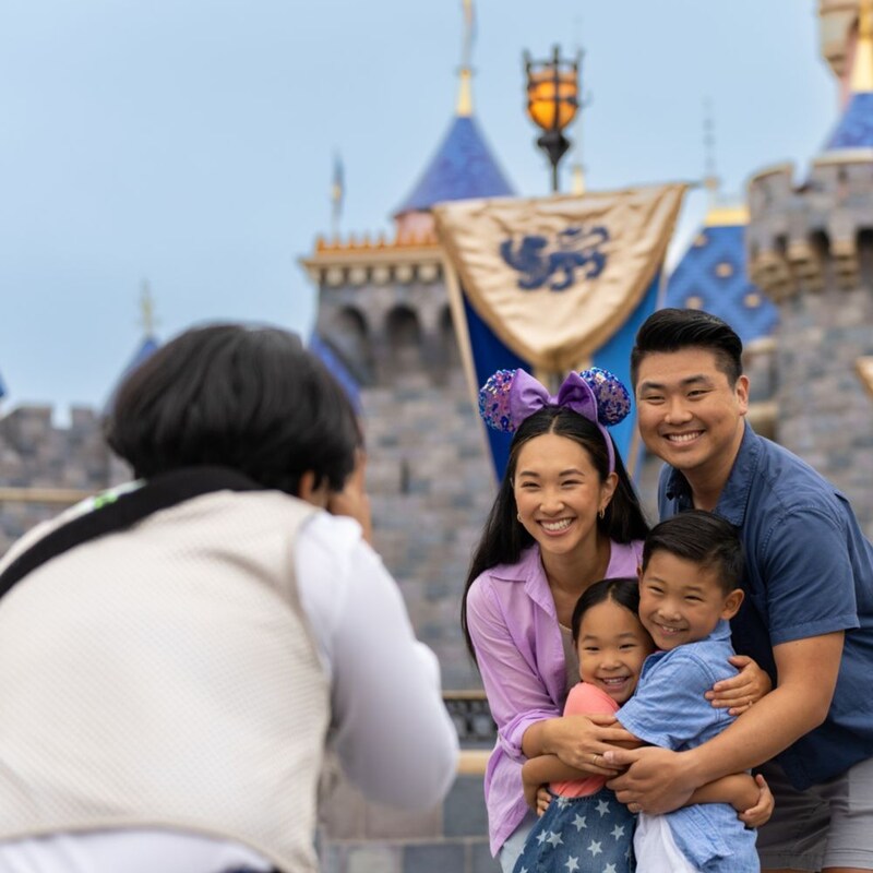Un fotógrafo de Disney PhotoPass tomando una foto de una familia frente al castillo Sleeping Beauty Castle