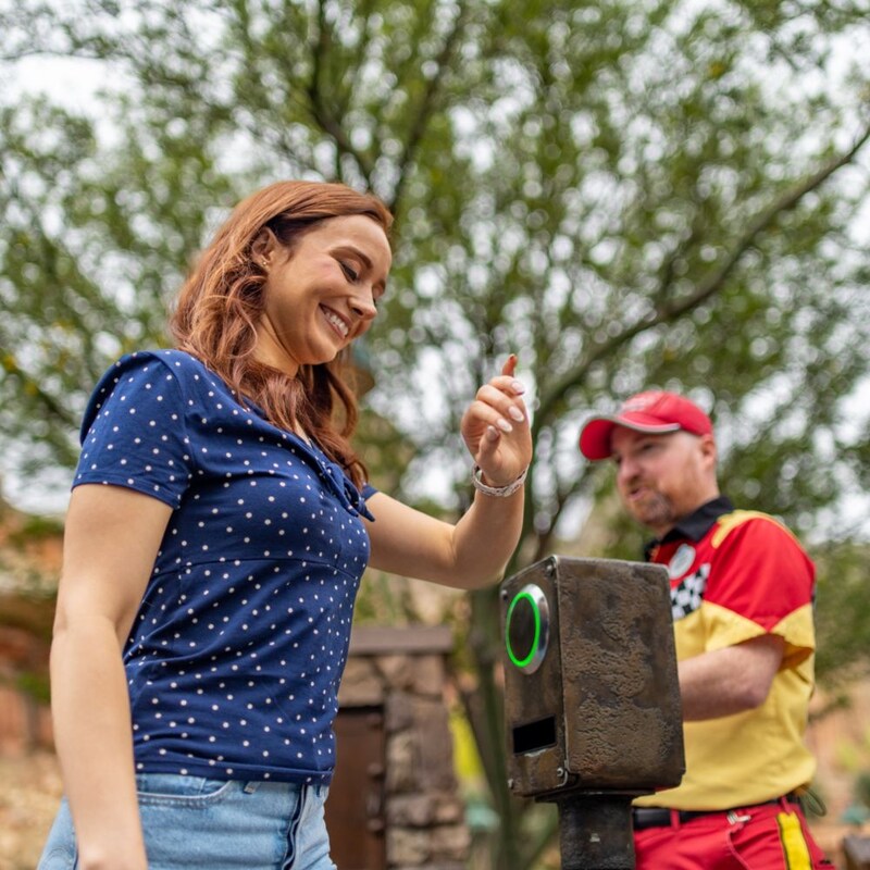 Una mujer sonriente tocando un punto de contacto con una pulsera Magic Band Plus