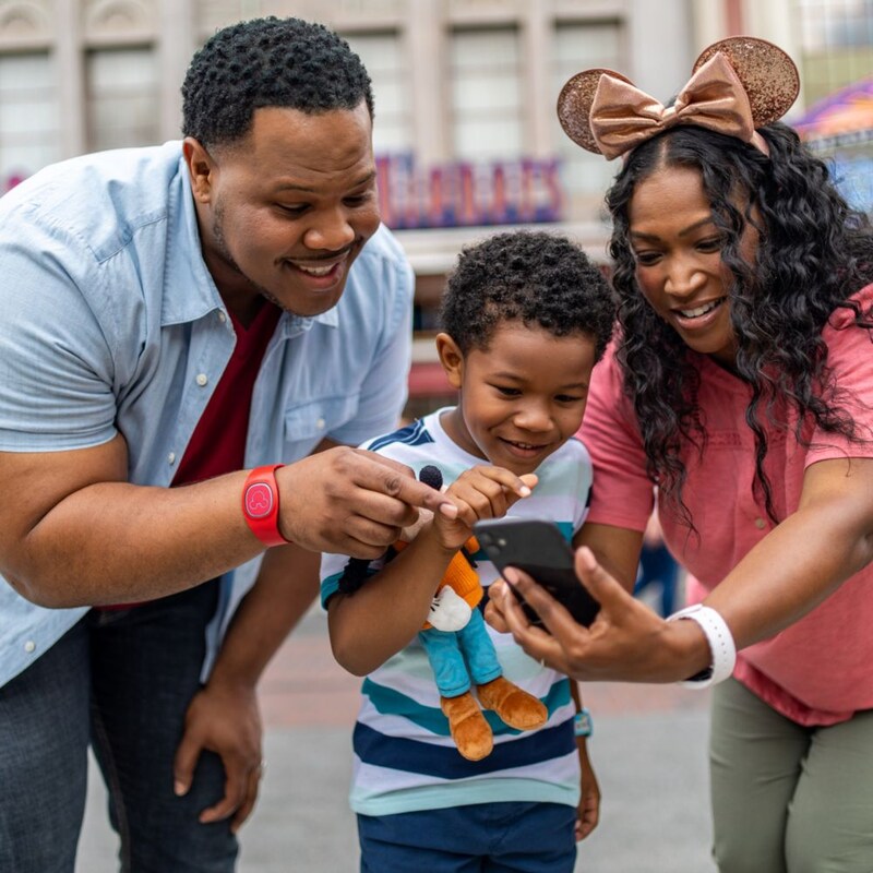 Dos adultos y un niño con pulseras Magic Band Plus y que miran un teléfono