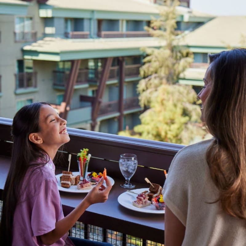 A family dining together on a hotel balcony overlooking the grounds of Disney’s Grand Californian Hotel & Spa