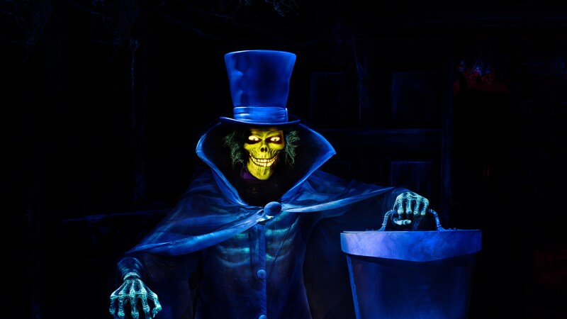 Hatbox Ghost de la atracción Haunted Mansion sosteniendo una sombrerera, con su espeluznante rostro resplandeciente