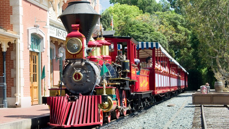 El tren de Disneyland Railroad detenido en la estación de Main Street con Visitantes en vagones de pasajeros al aire libre