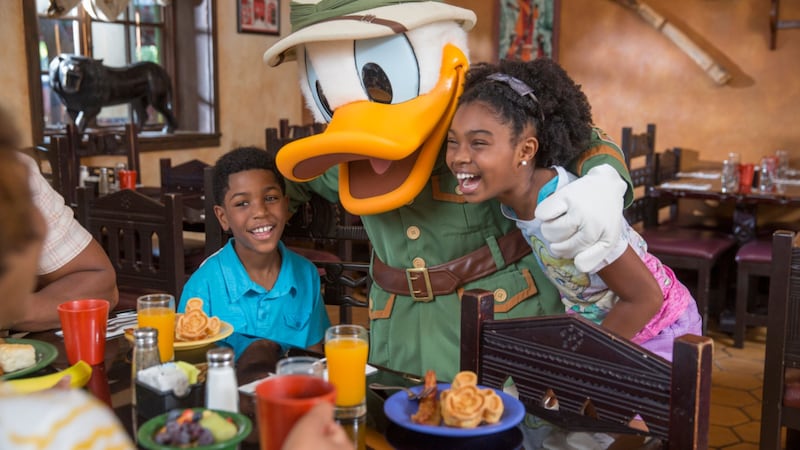 Donald Duck hugs 2 kids next to a breakfast table