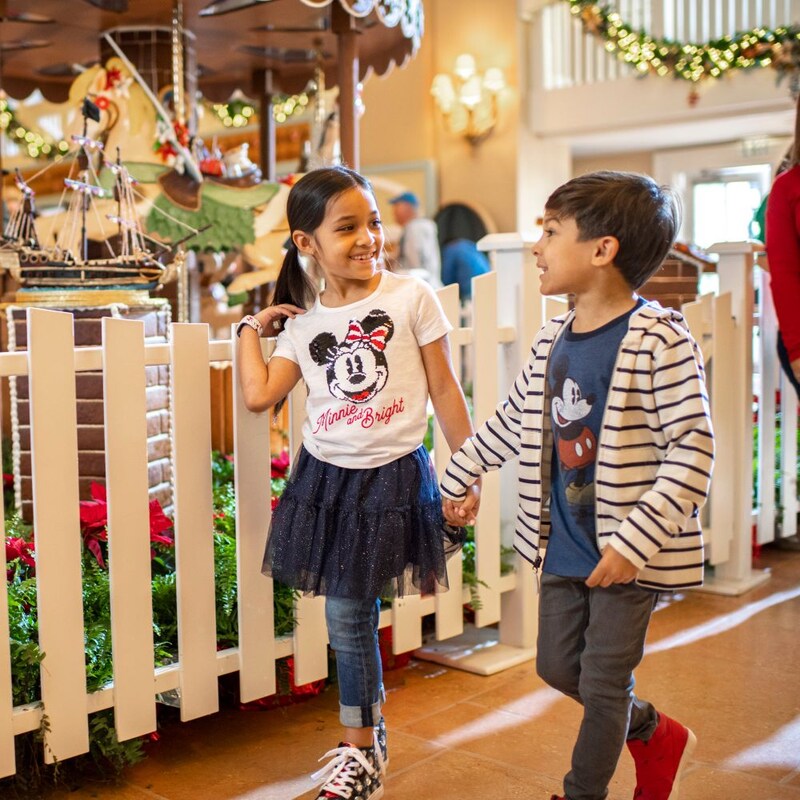 Two young children holding hands while walking near the Gingerbread Carousel at Disney's Beach Club Resort