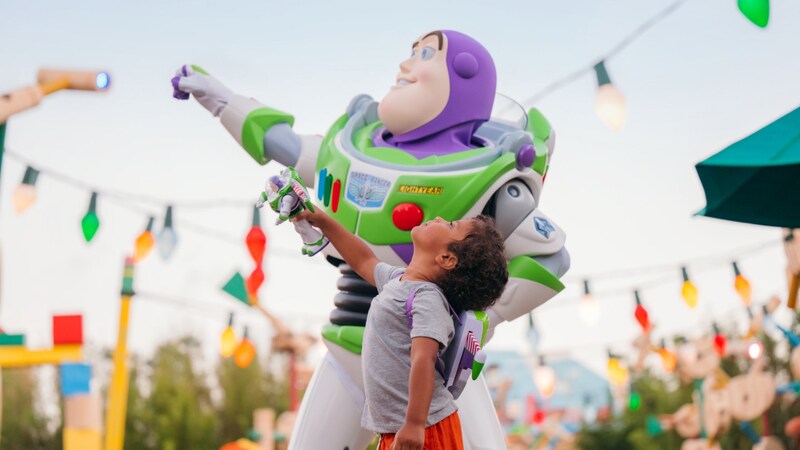 A boy standing next to Buzz Lightyear in Toy Story Land
