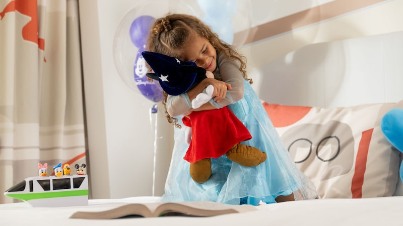  A girl on a bed hugging a Sorcerer Mickey Mouse plush toy