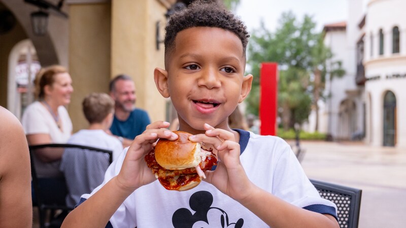  A boy holding a sandwich and smiling with his mother and sister at The Polite Pig restaurant
