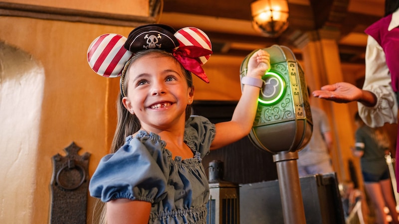  A young girl in a Minnie Mouse ear headband tapping her MagicBand as a Cast Member looks on