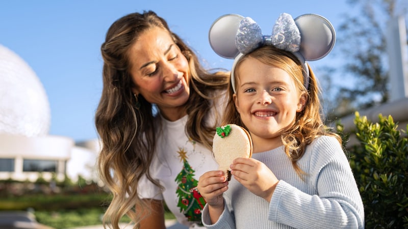  A young girl in a Minnie Mouse ear headband sitting with her mother while holding a cookie