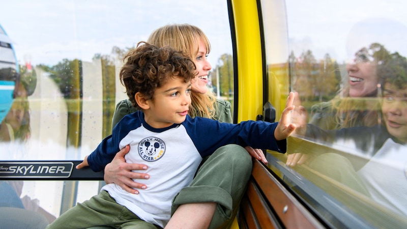  A young boy  with his mother pointing out the window of a Disney Skyliner gondola