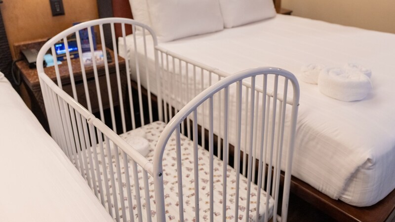  A crib positioned beside a bed in a hotel room